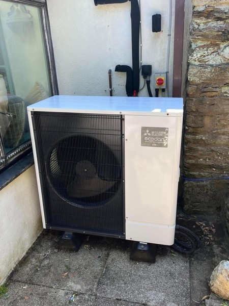 Mitsubishi Electric Ecodan outdoor air-source heat pump beside a stone wall with insulated pipework behind it