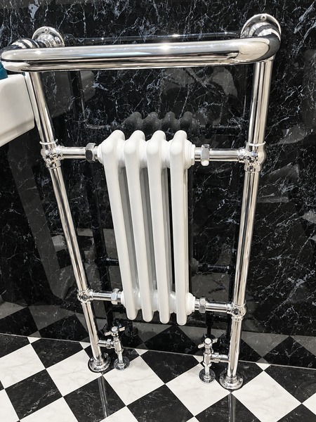 Chrome towel rail surrounding a white column radiator against a black marble-patterned wall