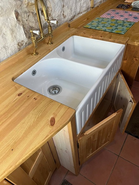 White double-bowl ceramic kitchen sink with a brass bridge tap set into a timber worktop