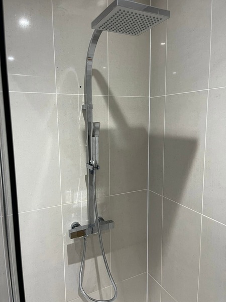 Chrome shower with a square rainfall head, handheld attachment and bar mixer against light grey tiles