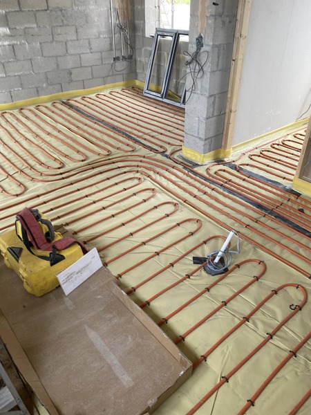 Orange underfloor heating pipes clipped in loops across insulated floors during building work