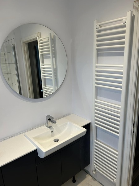 White basin with a chrome mixer tap on a dark vanity unit, round mirror and tall white towel radiator