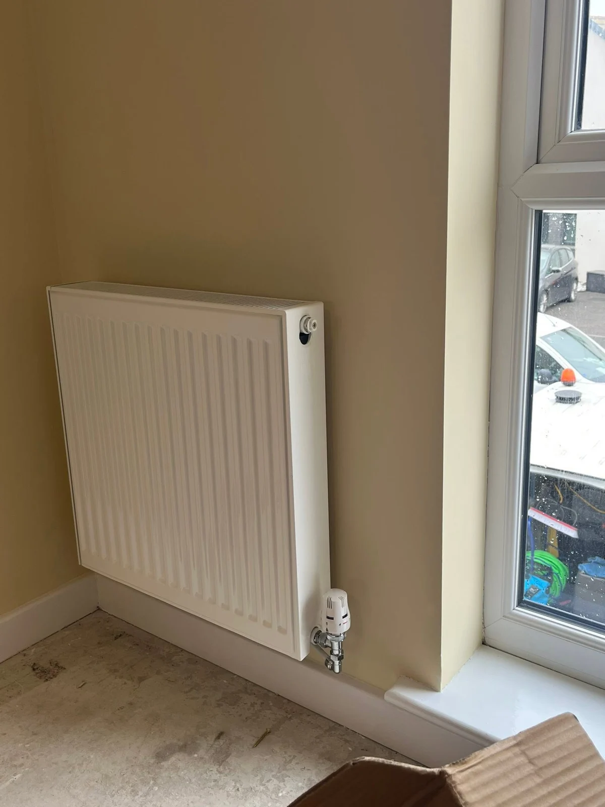 Compact white radiator fitted to a wall beside a window